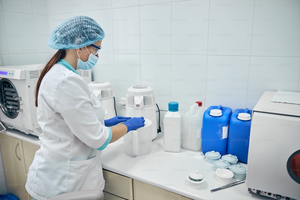 Side view of doctor assistant in protective mask and blue gloves in hands cleaning equipment after manipulation on patient