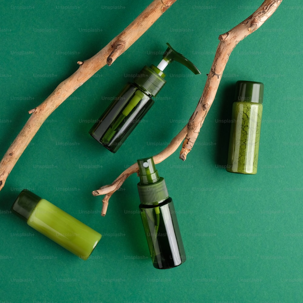 Umweltfreundliche Kosmetikprodukte auf grünem Hintergrund. Draufsicht grüne Glasflaschen und Holzzweig. Verpackungsdesign für natürliche Bio-Schönheitsprodukte.