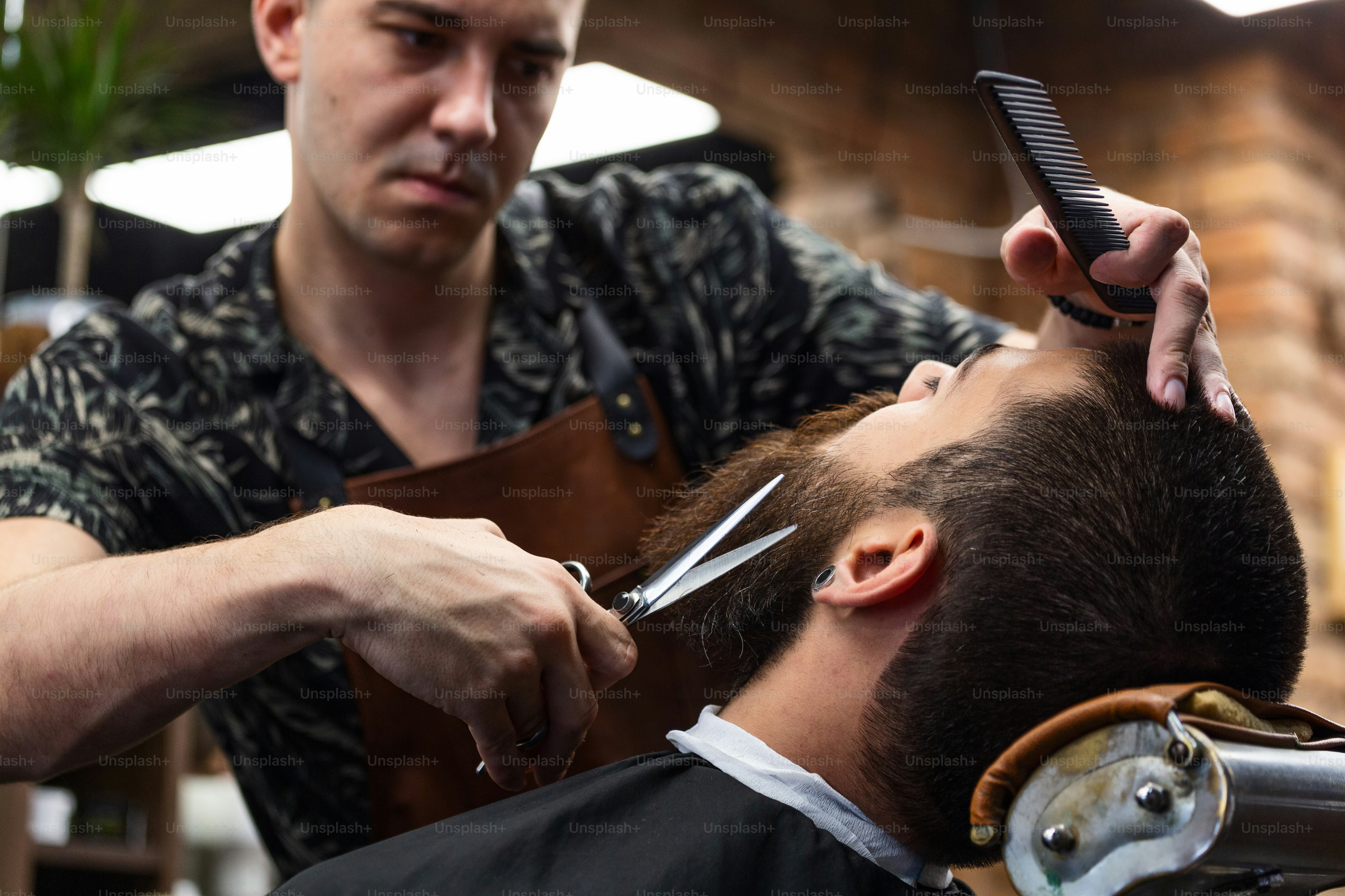 Close up cropped photo of a hairdresser`s work for an attractive guy at the barber shop. He is doing styling of his beard with scissors