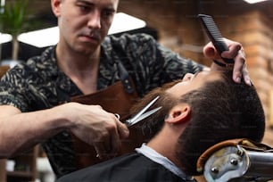 Close up cropped photo of a hairdresser`s work for an attractive guy at the barber shop. He is doing styling of his beard with scissors