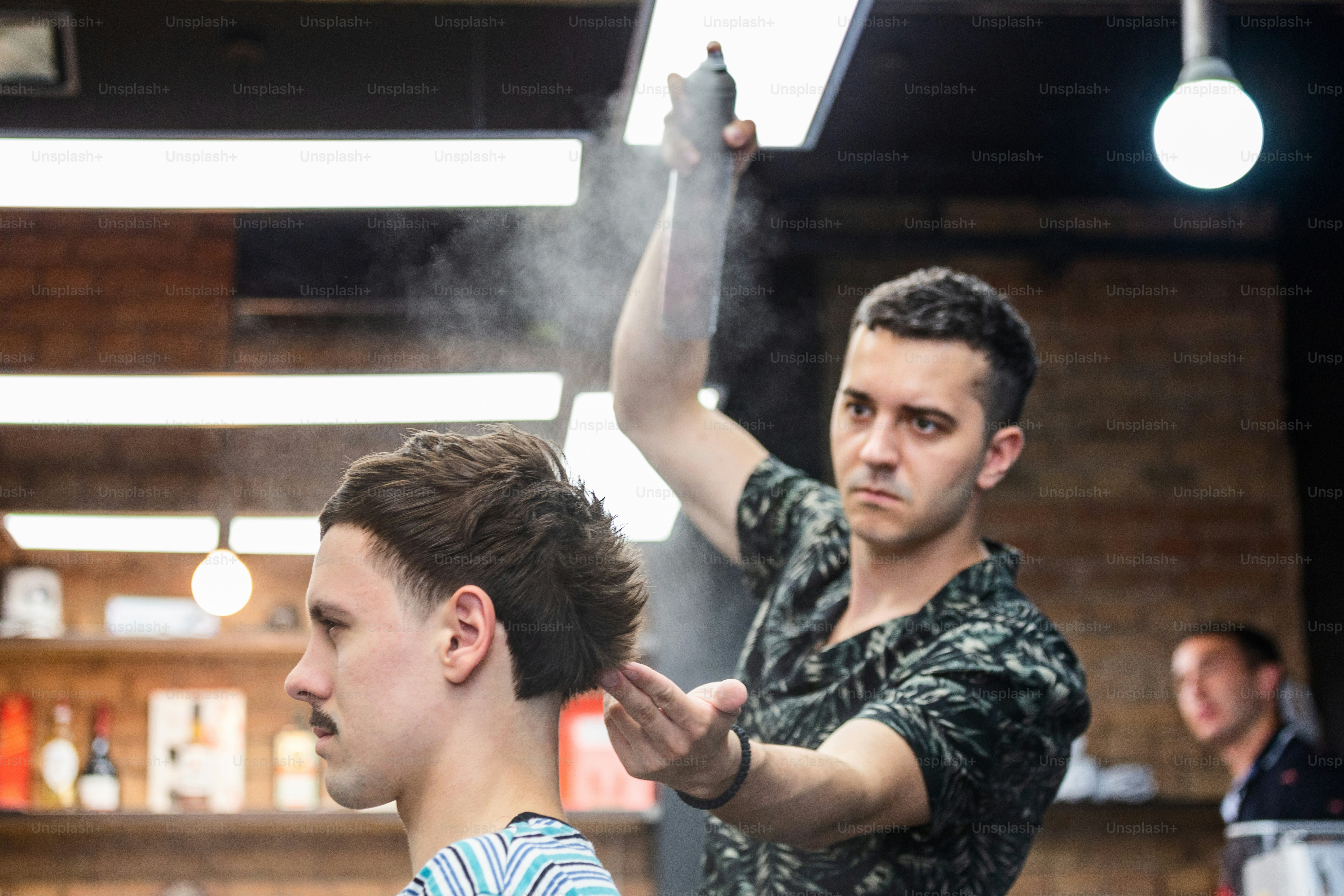 Professional Hairdresser using hair spray on client hair at barber shop