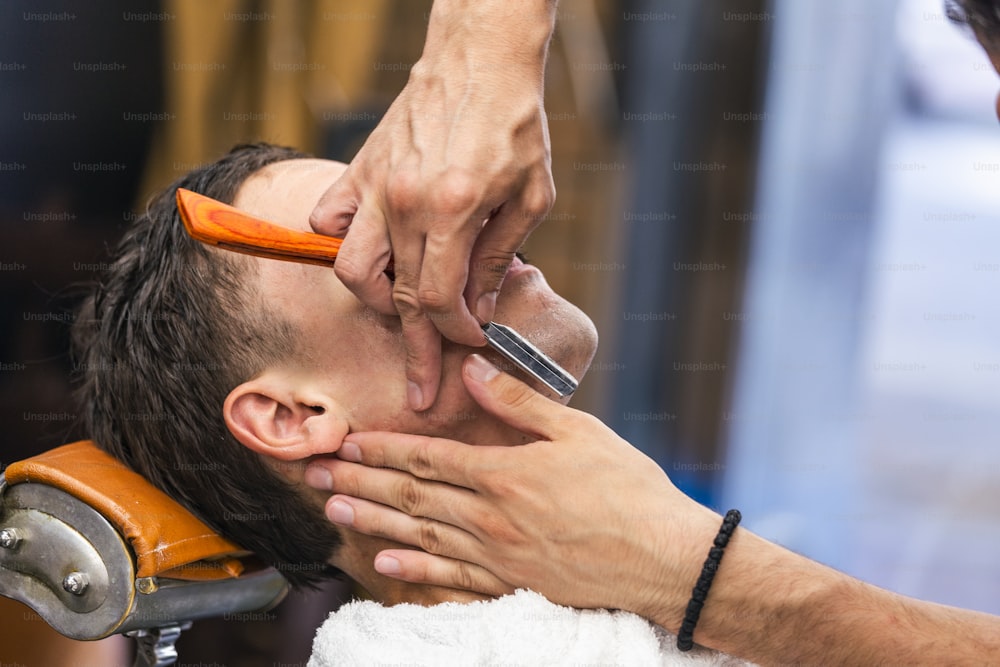 Rasiermesser in den Händen eines spezialisierten Friseurs. Friseur rasiert einen Mann in einem Friseursalon, Nahaufnahme. Mann Mith Schnurrbärte mit einer Rasur