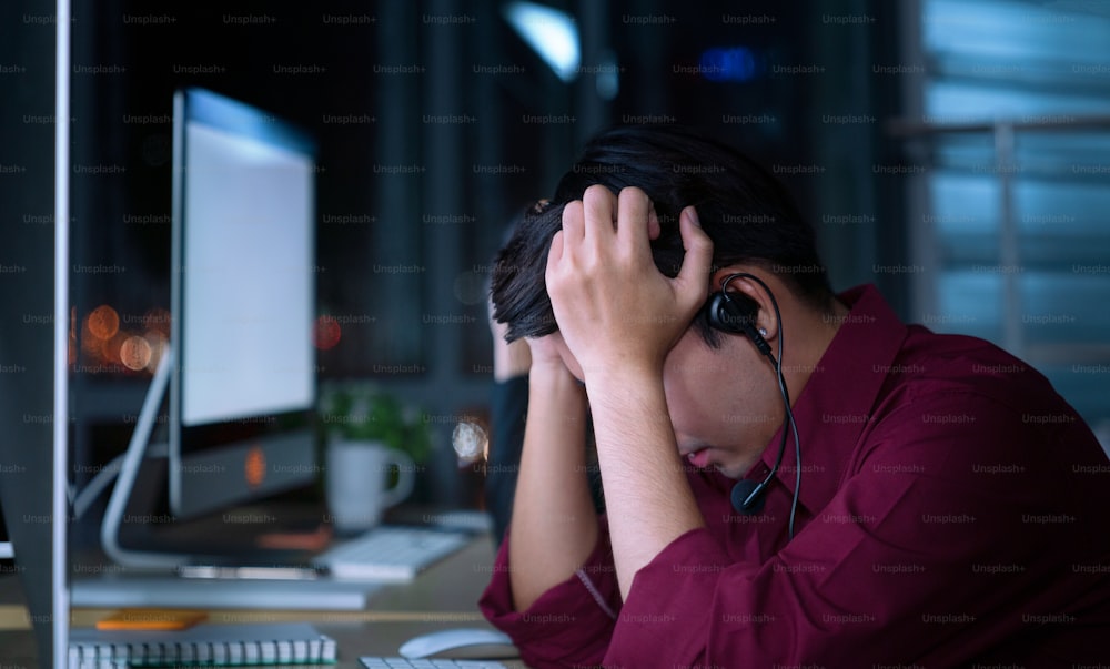 Thai asian call center business people get headache and migraine from working late night shift for helping assistance customer in workplace at night time
