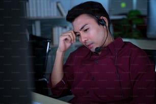 Gli uomini d'affari asiatici tailandesi del call center ottengono mal di testa ed emicrania dal lavoro a tarda notte per aiutare il cliente di assistenza sul posto di lavoro di notte