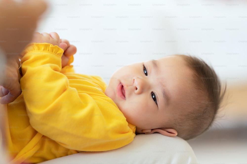 Süßes Baby mit Flasche auf dem Bett, thailändisches kleines asiatisches Kind liegt auf weißem Bett und trinkt Milch aus der Flasche