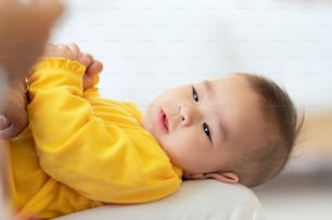 Bambino carino con il biberon sul letto, piccolo bambino asiatico tailandese sdraiato sul letto bianco che beve il latte dal biberon