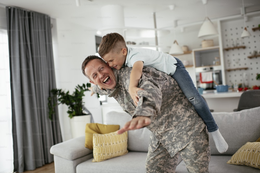 Soldado divirtiéndose con su hijo en casa. Padre e hijo jugando en la sala de estar.