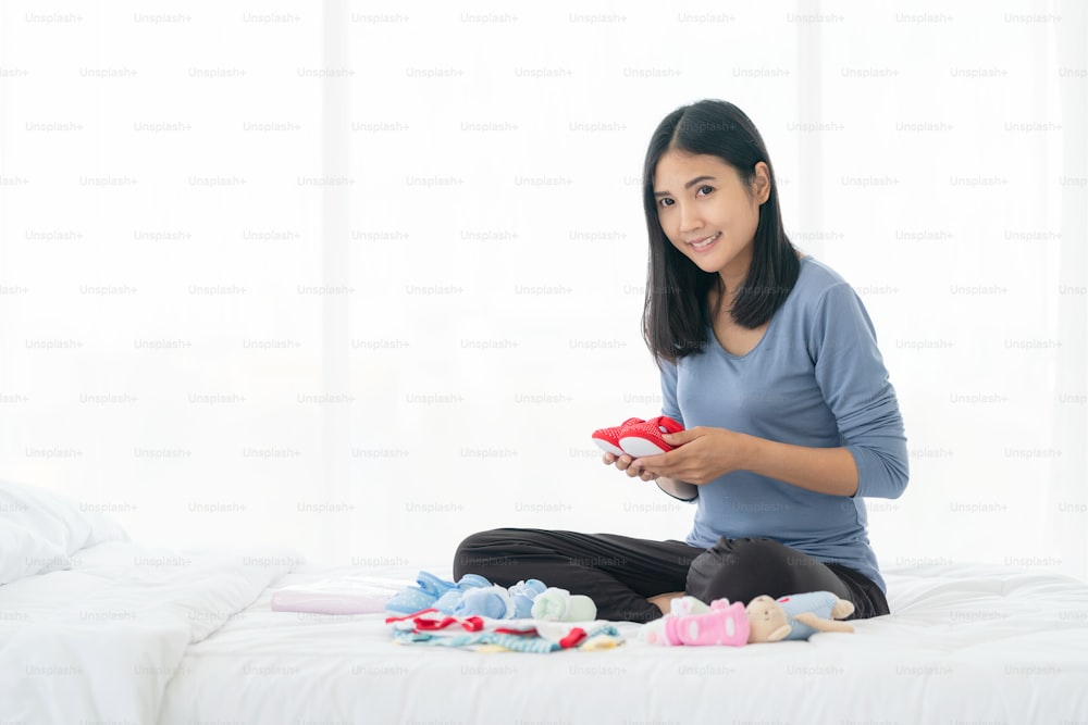 Woman packing baby accessories on bed. Baby clothes for newborn.