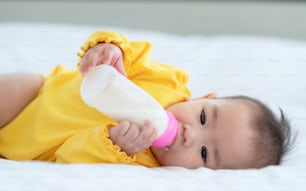 Cute baby with bottle on bed, Thai little Asian child lying on white bed drinking milk from bottle