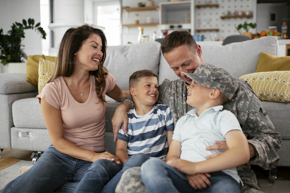 Happy soldier sitting on the floor with his family. Soldier and his wife enjoying at home with children.