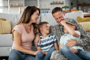 Happy soldier sitting on the floor with his family. Soldier and his wife enjoying at home with children.