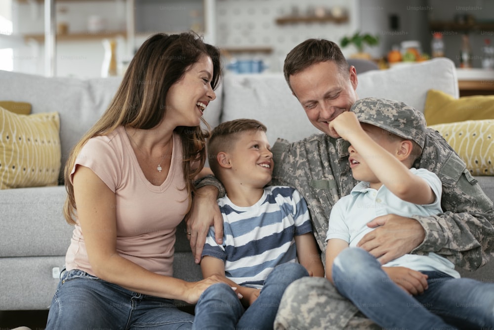 가족과 함께 바닥에 앉아 있는 행복한 군인. 군인과 그의 아내는 아이들과 함께 집에서 즐기고 있습니다.
