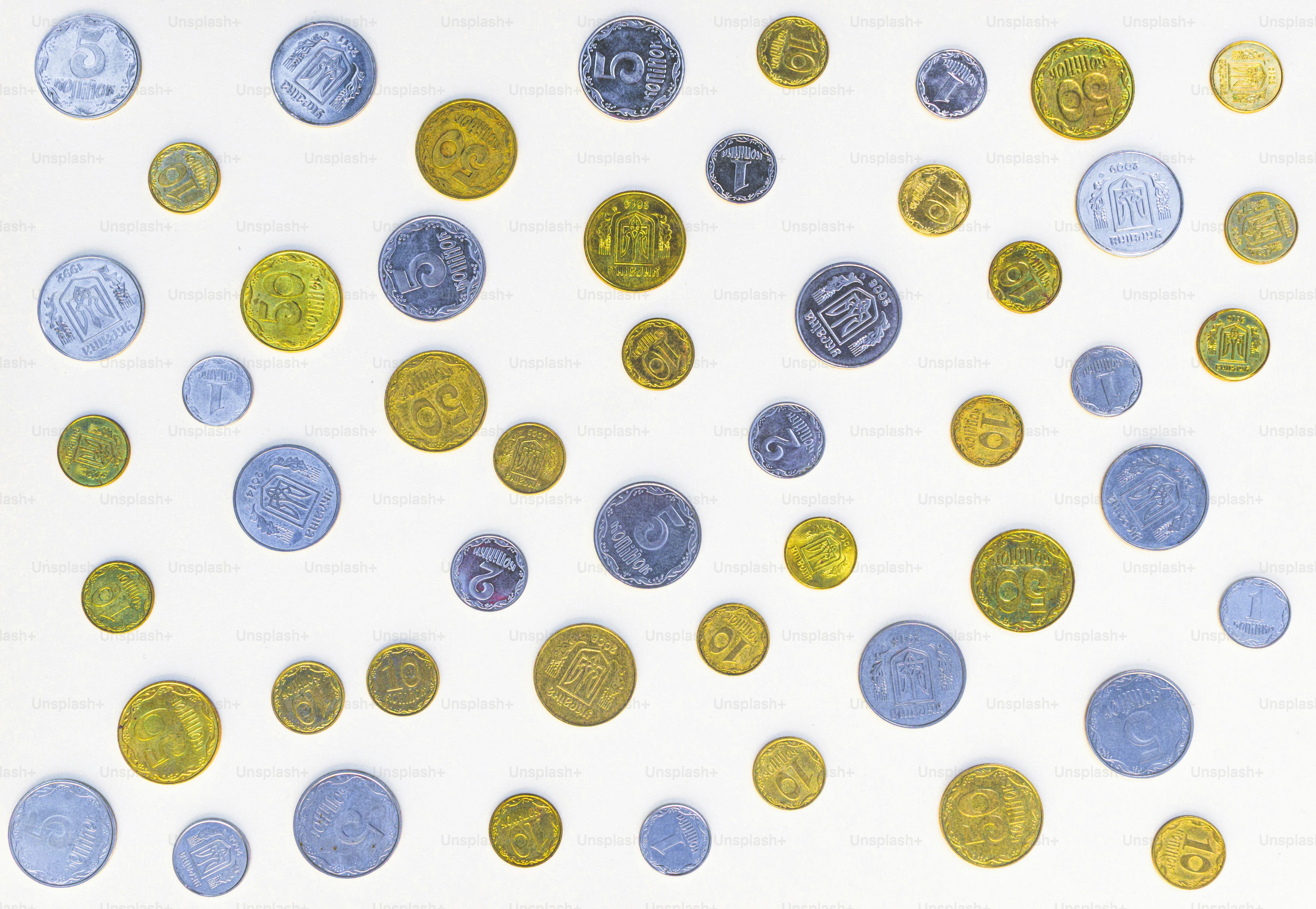 A collection of silver and gold Ukrainian coins scattered on a white surface