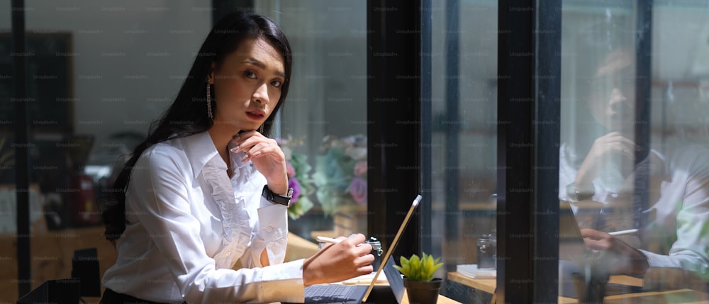 Retrato da trabalhadora olhando para a câmera enquanto trabalha on-line no espaço de trabalho portátil no café