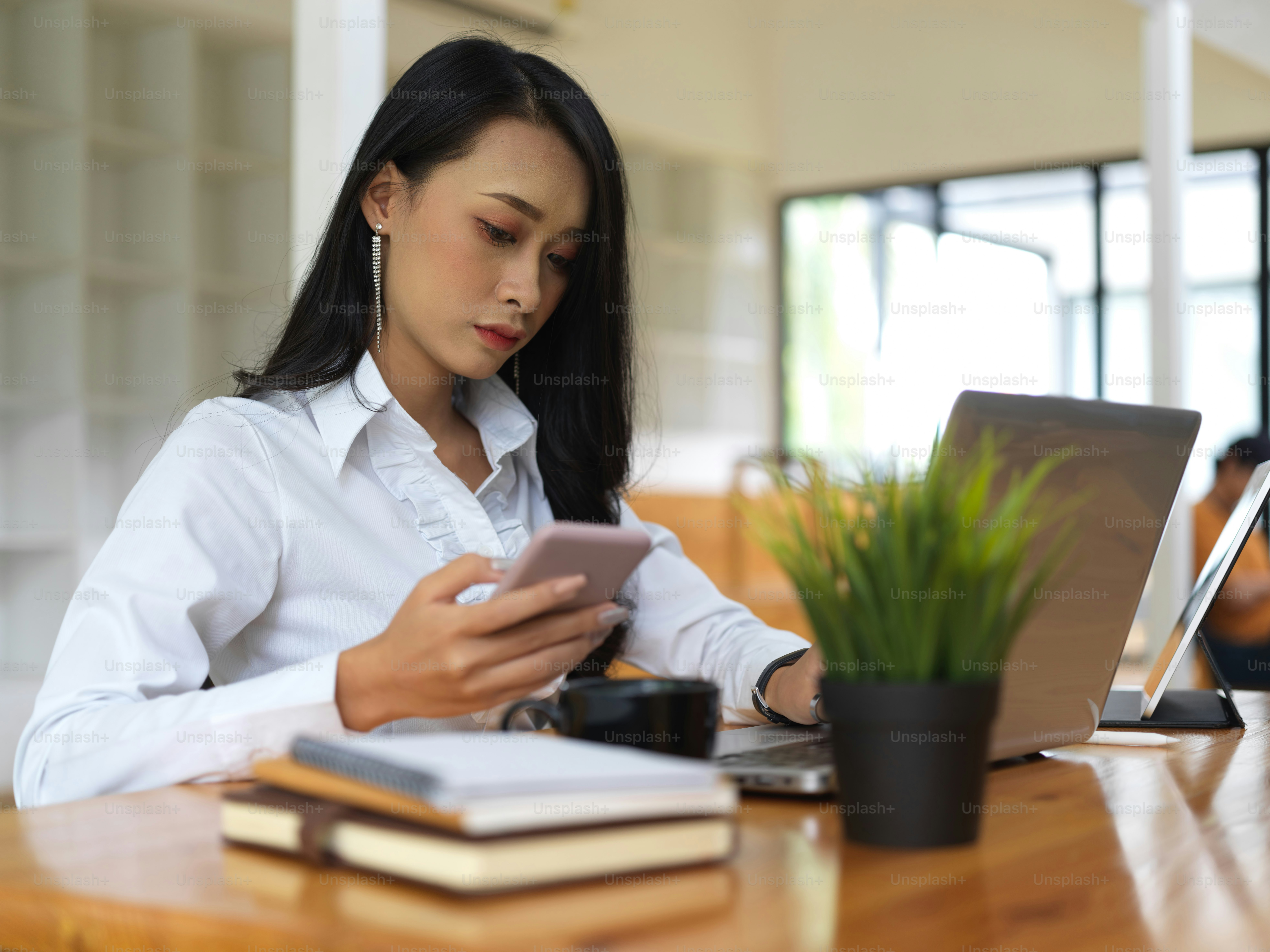 Potret wanita yang bekerja dengan smartphone, laptop, dan buku di ruang kerja bersama