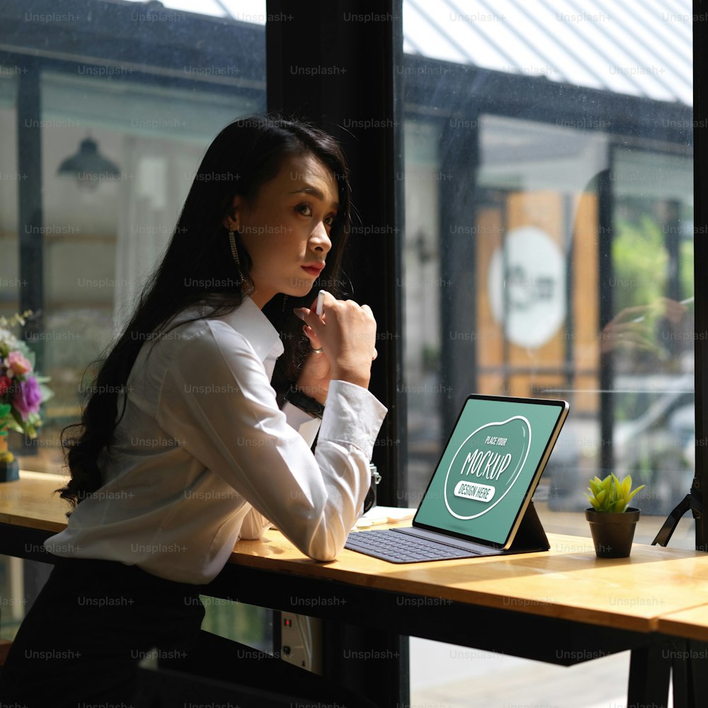 Cropped shot of thoughtful female office worker sitting with mock up digital tablet on wooden bar in cafe