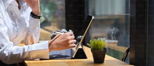 Vue latérale de la main féminine à l’aide d’une tablette numérique avec un stylet sur une table en bois