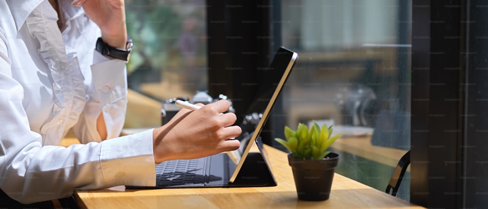 Seitenansicht der weiblichen Hand mit digitalem Tablet mit Eingabestift auf Holztisch