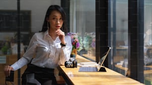 Portrait d’une jeune femme indépendante séduisante assise à un bar en bois avec un appareil photo et une tablette numérique dans un café