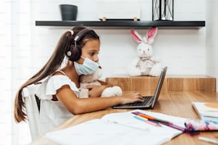 Covid-19 전염병 위기 잠금 또는 격리 기간 동안 e-러닝 세션을 갖는 어린 소녀. 질병 예방 및 새로운 정상 개념.