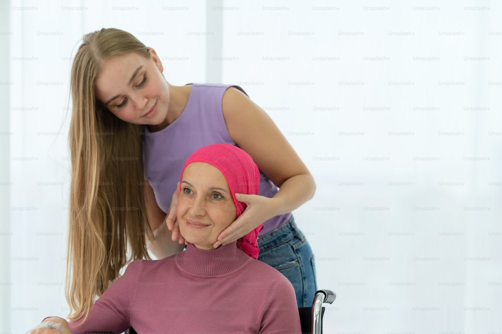 Young daughter embracing her sick mom who wearing headscarf on wheelchair, giving support battling through cancer.