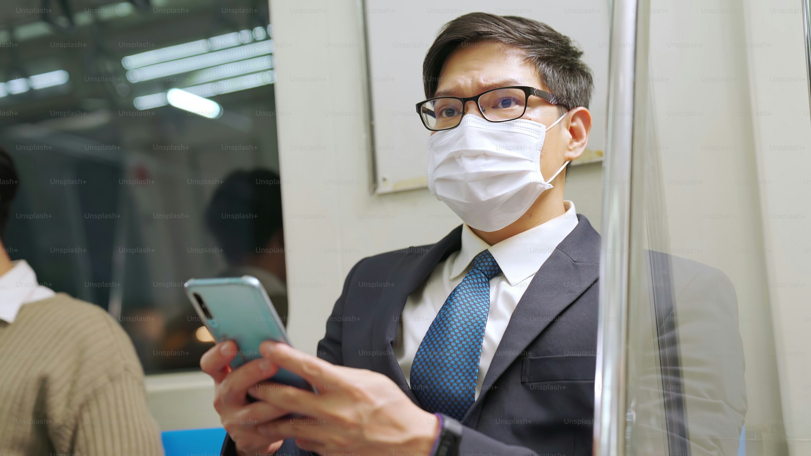 Traveler wearing face mask while using mobile phone on public train . Coronavirus disease or COVID 19 pandemic outbreak and urban city lifestyle problem in rush hour commuting concept .