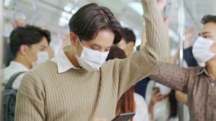 Traveler wearing face mask while using mobile phone on public train . Coronavirus disease or COVID 19 pandemic outbreak and urban city lifestyle problem in rush hour commuting concept .