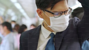 Young man wearing face mask travels on crowded subway train . Coronavirus disease or COVID 19 pandemic outbreak and urban lifestyle problem in rush hour concept .