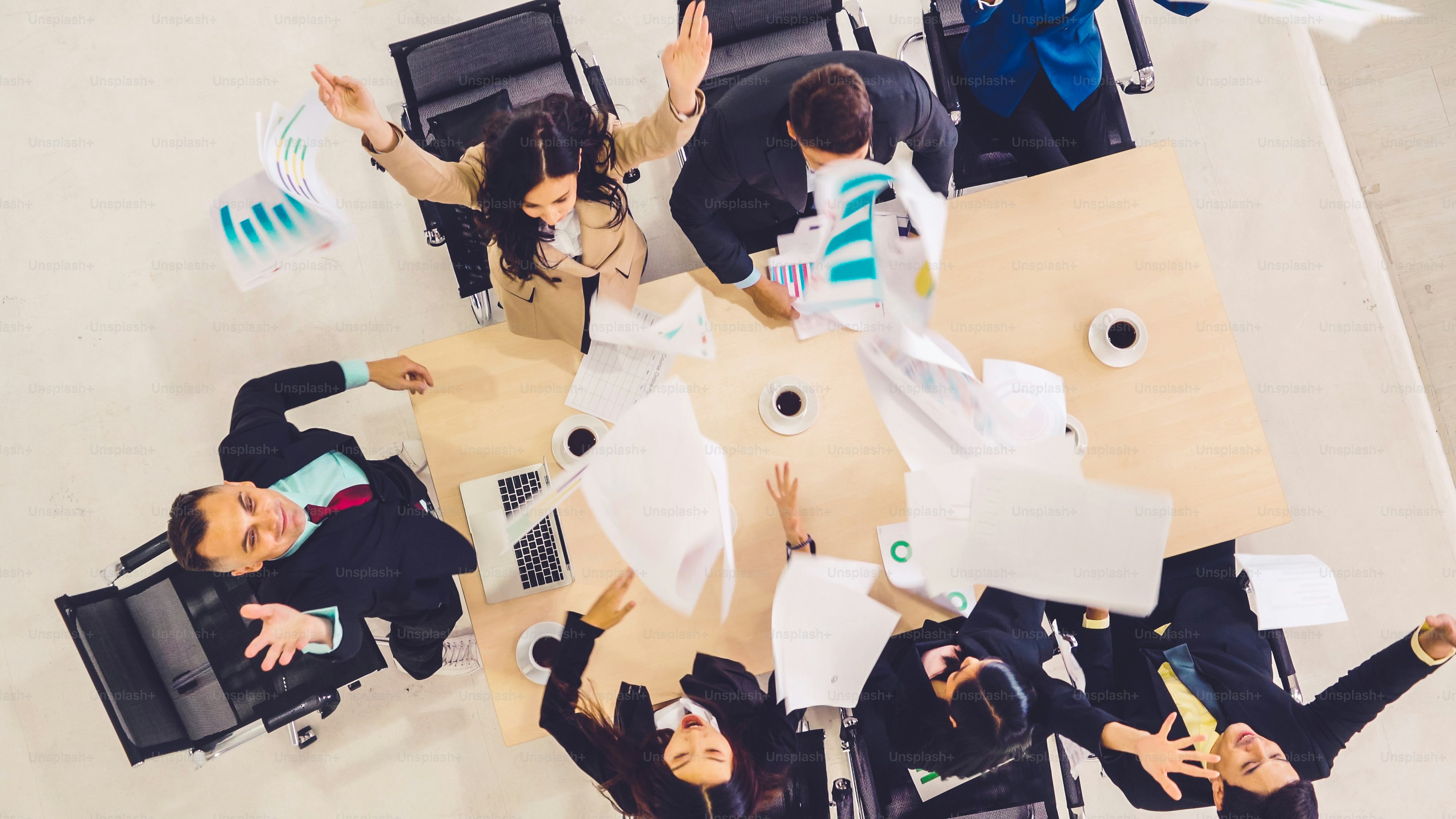 Erfolgreiche Geschäftsleute feiern gemeinsam mit Freude am Bürotisch von oben aufgenommen. Junge Geschäftsleute und Geschäftsfrauen drücken fröhlichen Sieg aus und zeigen Erfolg durch Teamarbeit.