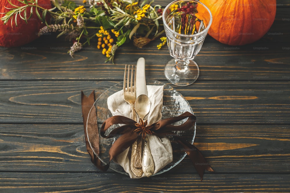 Mise en place de la table du dîner de Thanksgiving. Assiette élégante avec des couverts et des décorations d’automne, citrouille, branches naturelles et fleurs automnales sur une table rustique. Traiteur de mariage d’automne