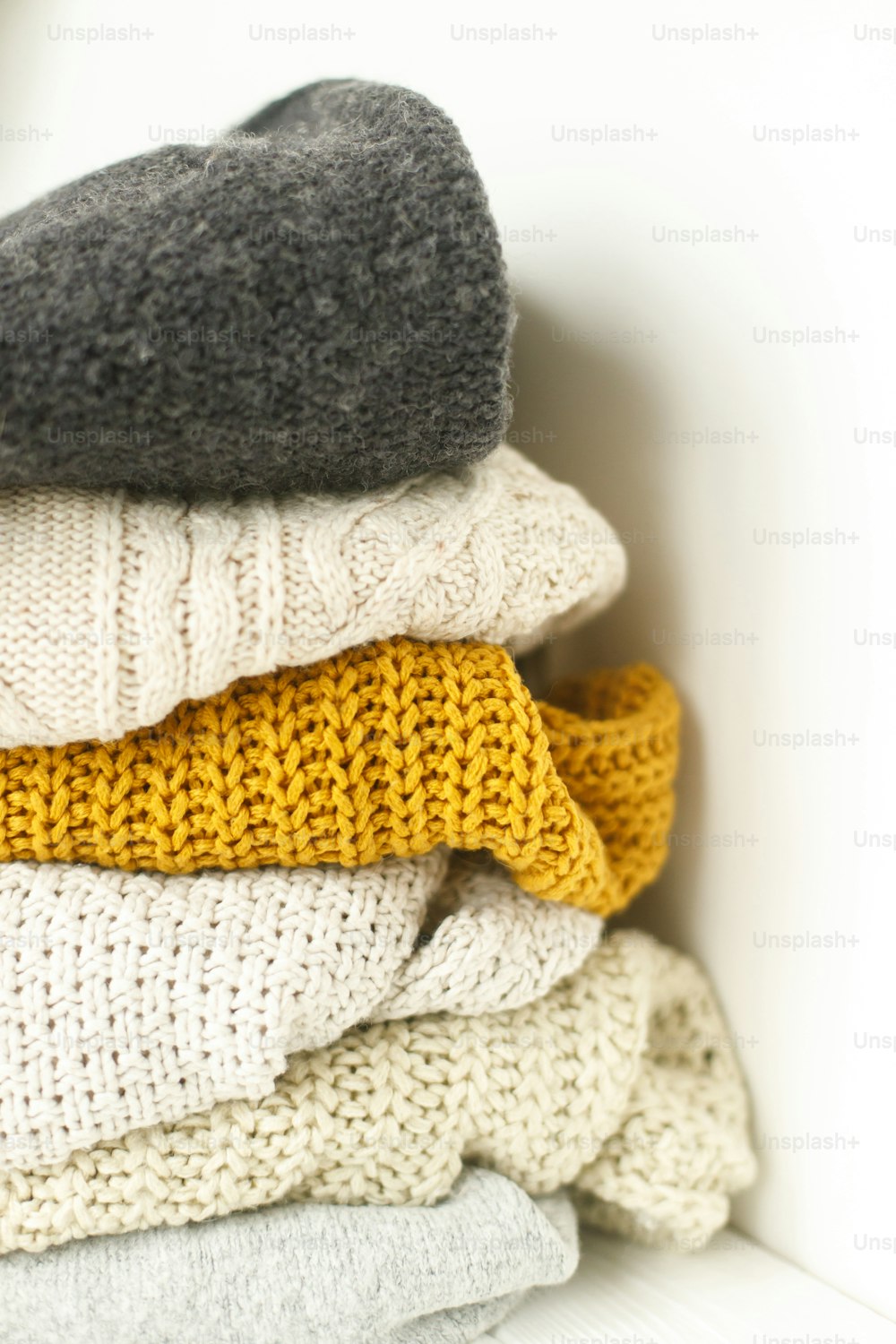 Cozy knitted sweater stack for cold autumn weather on white background. Stylish white, yellow and grey sweaters close up with space for text. Hello fall!