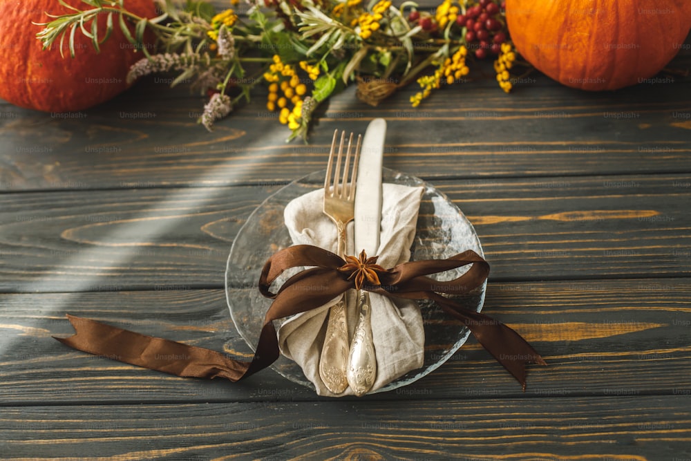 廃棄物ゼロの感謝祭のディナー。素朴なテーブルの上にカトラリーと秋の装飾、カボチャ、自然の枝、秋の花が描かれたスタイリッシュなプレート。秋の結婚式