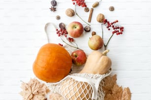 Reusable shopping bag with pumpkins, apples, berries, nuts and autumn leaves on white wooden background. Eco friendly Thanksgiving, flat lay. Zero waste holidays, fall harvest