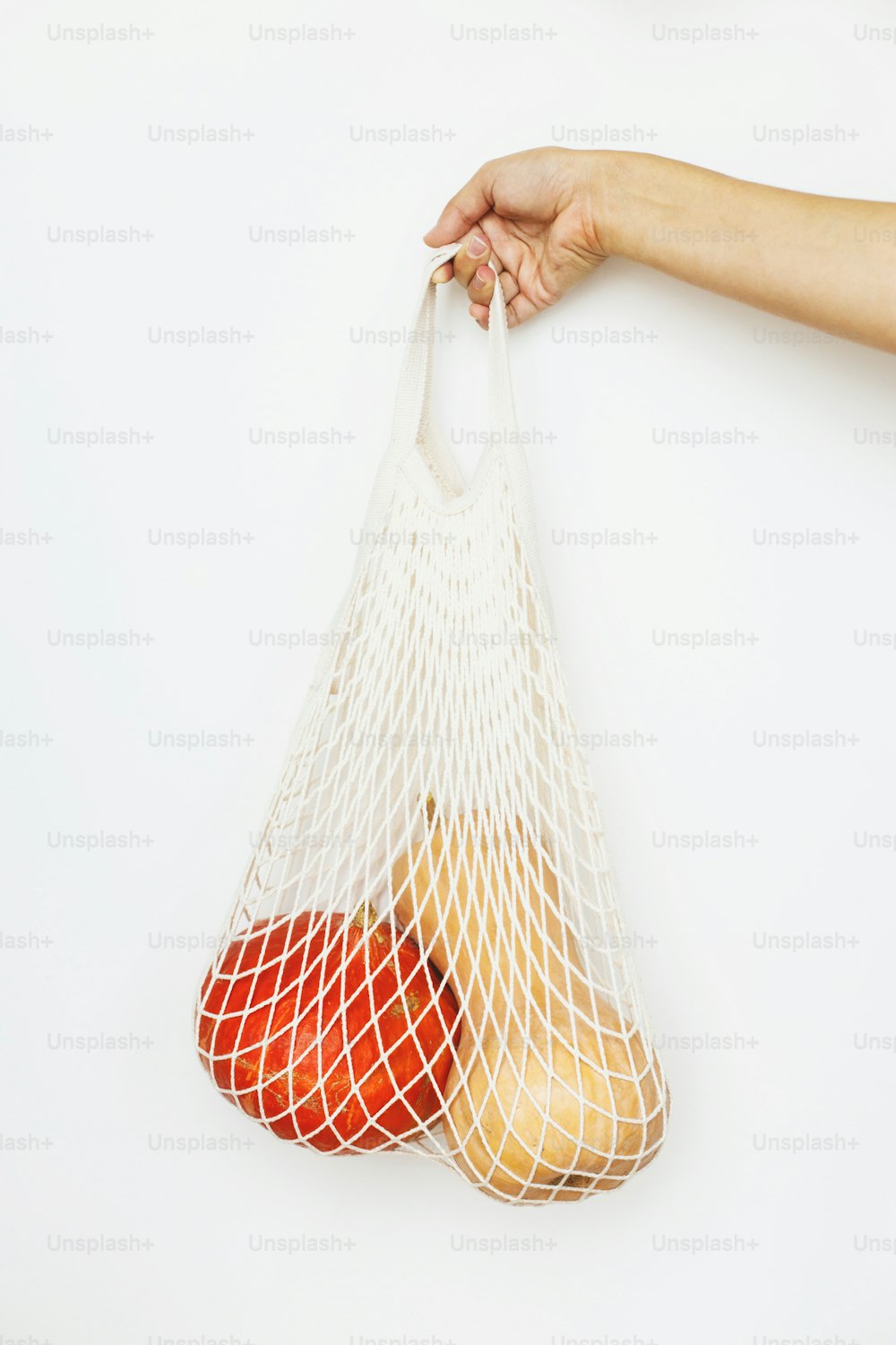 Eco friendly autumn holidays. Female hand holding reusable shopping bag with pumpkins on white background. Fall harvest