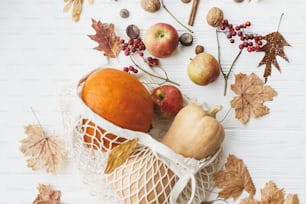 흰색 나무 배경에 호박, 사과, 딸기, 견과류, 단풍이 있는 재사용 가능한 쇼핑백. 친환경 추수감사절. 제로 웨이스트 휴일, 가을 수확