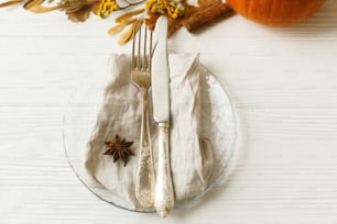 Stilvolle und abfallfreie Thanksgiving-Tischdekoration. Teller mit Besteck, Leinenserviette, Anis und Herbstlaub, Kürbis, Herbstblumen auf weißem Tisch. Rustikale Herbst-Hochzeitstischgarnitur.