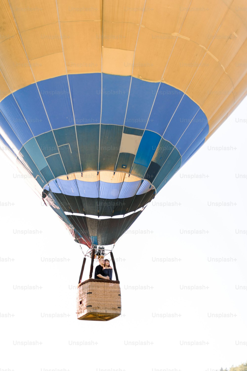 Beautiful romantic couple hugging in the basket of hot air balloon, flying in summer sunny evening. Romantic adventure, love in flight concept. View from land.