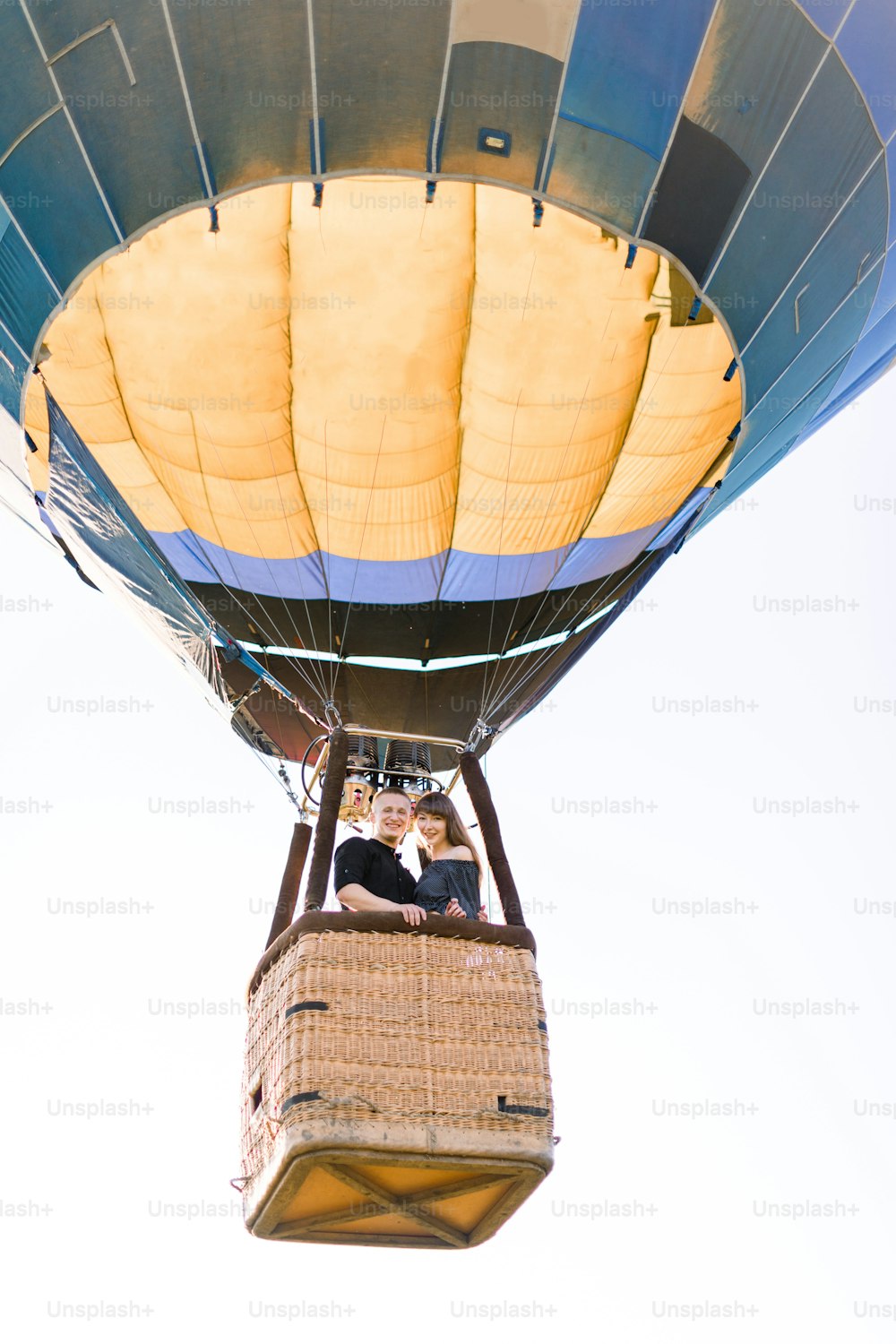 Beautiful romantic couple hugging in the basket of hot air balloon, flying in summer sunny evening. Romantic adventure, love in flight concept. View from land.