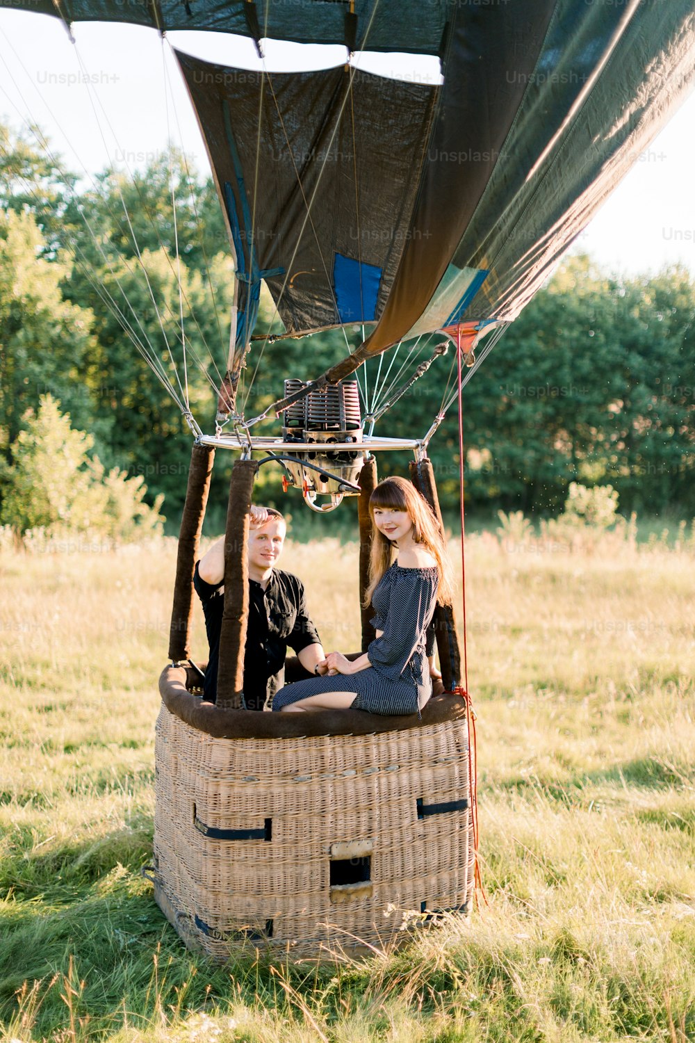 Romantic date, marriage proposal, engagement, wedding anniversary concept. Couple in love sitting in the basket of hot air balloon on the background of summer sunny field.