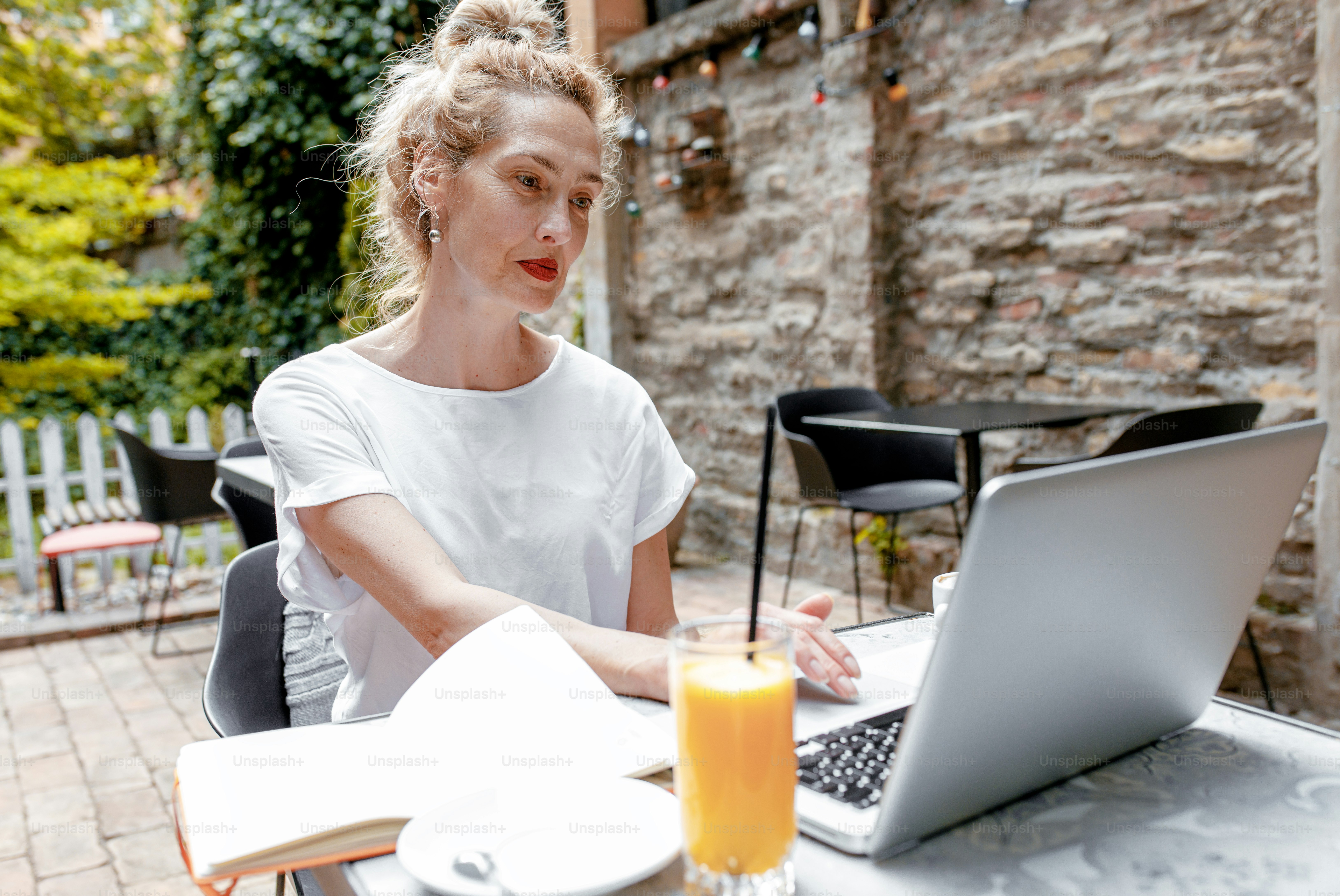 Ältere Bloggerin in Freizeitkleidung sitzt im Café mit Laptop