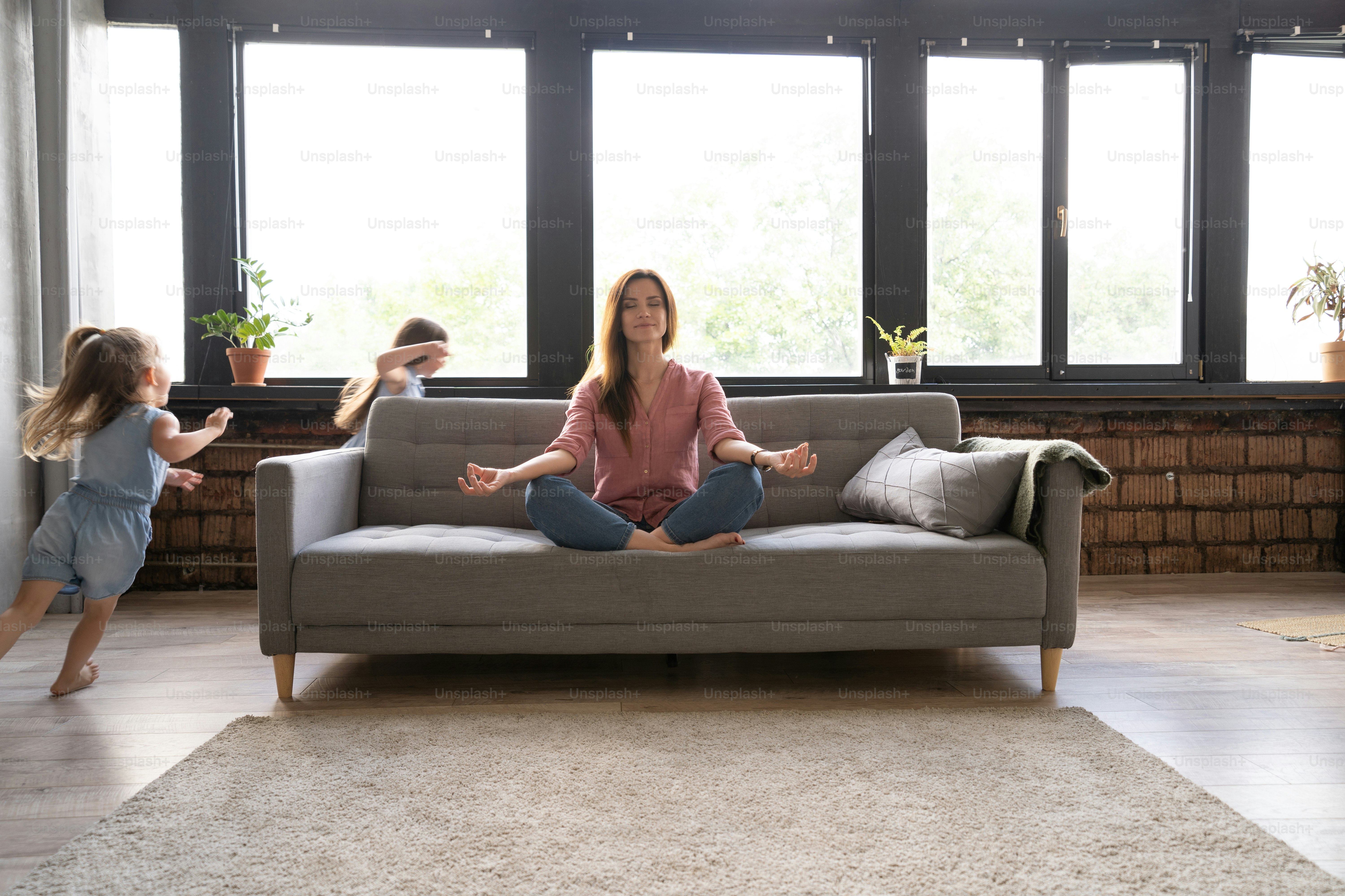 Calm woman concentrating on yoga exercises on couch at home while two ...