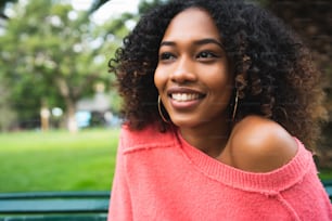 Portrait of young beautiful afro american woman sitting on bench in the park. Outdoors.