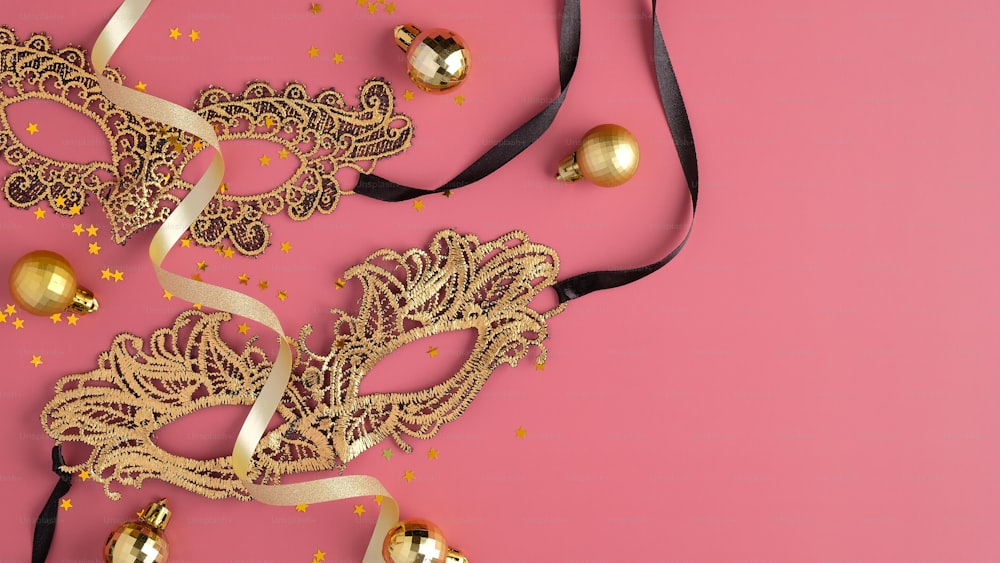 金色の仮面舞踏会のマスク、パーティーの吹き流し、パステルピンクの背景にクリスマスボールの装飾。フラットレイ、上面図。クリスマスやカーニバルパーティーのための豪華なスタイルのバナーモックアップ