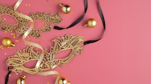 Goldene Maskenmasken, Partystreamer, Weihnachtskugeln Dekorationen auf pastellrosa Hintergrund. Flache Lage, Draufsicht. Luxus-Banner-Mockup für Weihnachts- oder Karnevalsparty