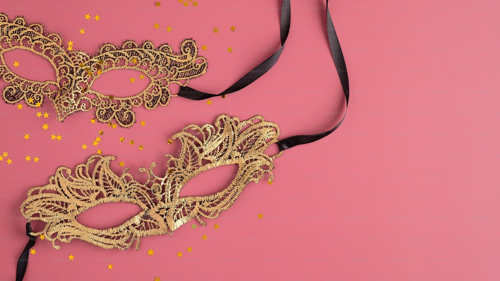 Goldene Faschingsmasken und Konfetti auf pastellrosa Hintergrund. Flache Lage, Draufsicht. Weihnachten, Maskerade Konzept