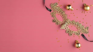 Golden masquerade mask and Christmas balls decorations on pastel pink background. Flat lay, top view. Christmas party banner mockup.