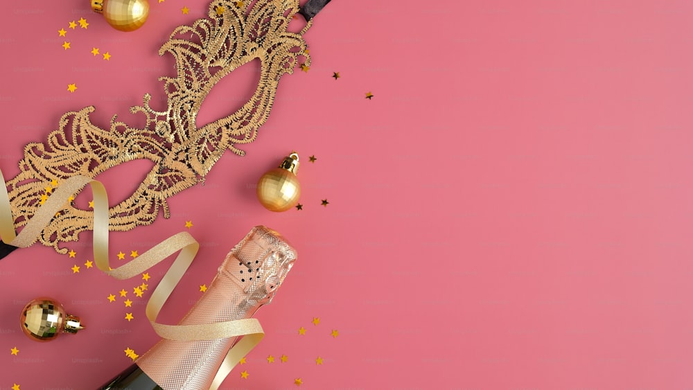 Weihnachtsfeier-Konzept. Goldene Balldekoration, Faschingsmaske, Sektflasche, Konfetti auf rosa Hintergrund. Flache Lage, Draufsicht.