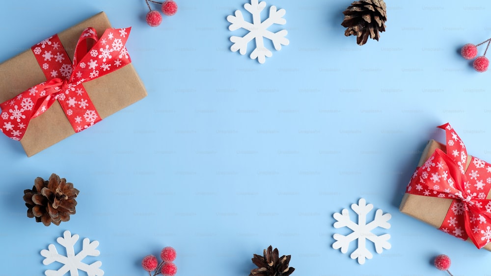 크리스마스 구성입니다. 수제 선물 상자, 나무 눈송이, 소나무 콘, 파란색 배경에 빨간색 열매로 만든 프레임. 플랫 레이, 평면도, 복사 공간.