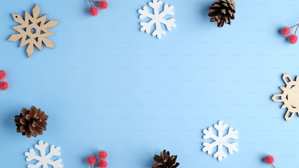 クリスマスカードのモックアップ。青い背景に木製の雪片、赤い果実、松ぼっくりのフラットレイ構図。クリスマス、冬休み、新年のコンセプト。