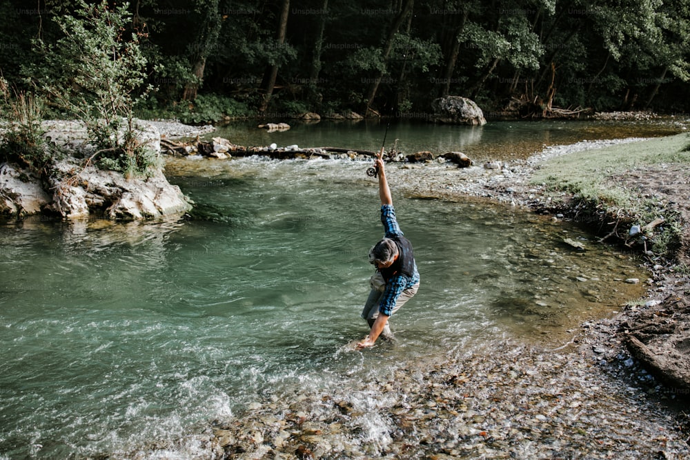 Senior man is fishing alone on fast mountain river. He is holding a live trout and kisses it before releasing it into the river again.